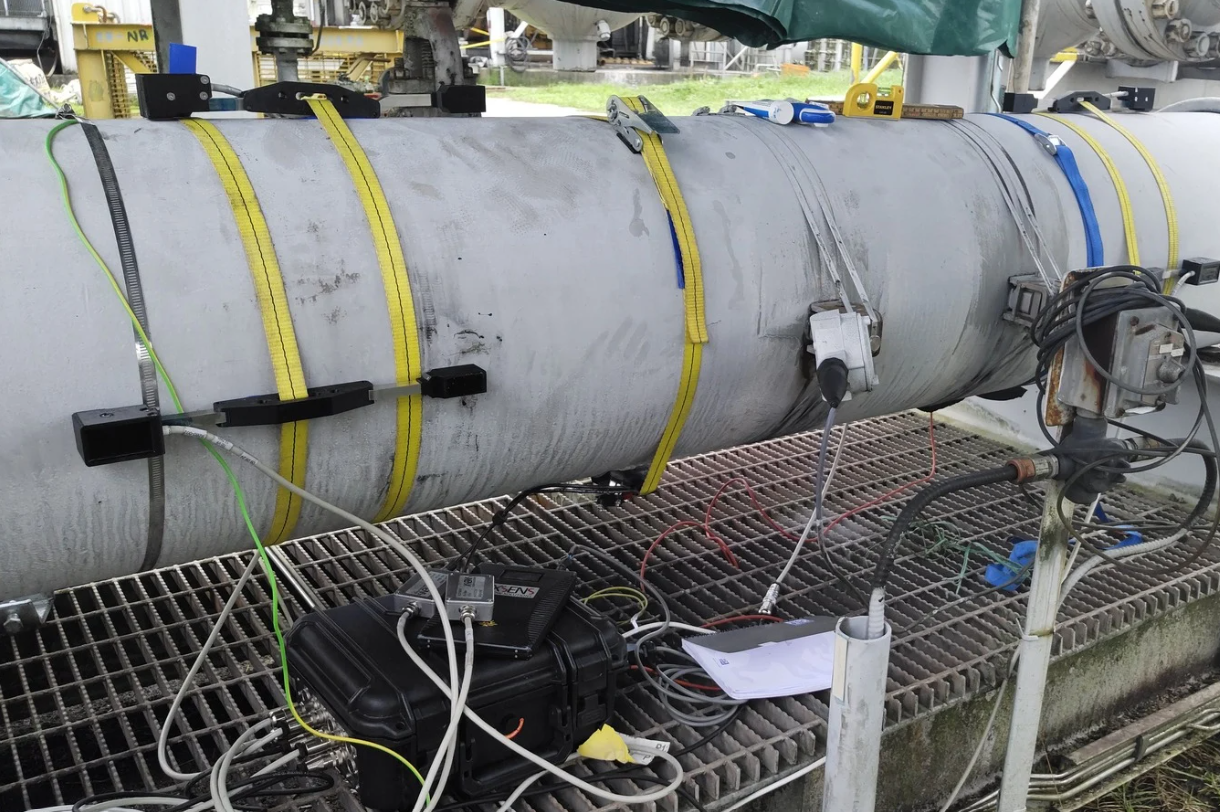 Onshore installation with portable kit showing transducers strapped to pipe, electronics pelicase, battery and PT100 temperature sensor.